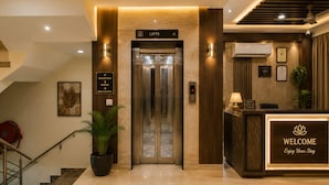 Zona de recepción de un hotel, con mostrador de recepción, pantalla digital del ascensor y una escalera que conduce a los pisos superiores.