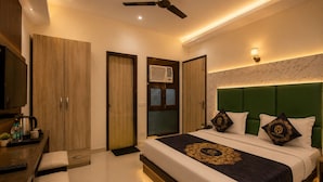 Habitación de hotel con cama, escritorio con hervidor, una silla, ventilador de techo y aire acondicionado de pared.