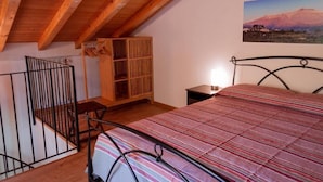 A bedroom with a sloped ceiling, a bed with a striped bedspread, a wooden cabinet, and a picture of a mountain on the wall. - Terre di Monacella (Santa Venerina)