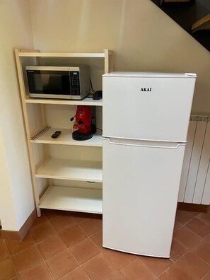 A compact kitchenette with a white refrigerator, a microwave, and a red coffee maker on a shelf. - Terre di Monacella (Santa Venerina)
