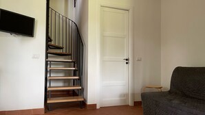 A staircase with wooden steps and black railings, a white door, and a grey sofa in a room with tiled flooring. - Terre di Monacella (Santa Venerina)