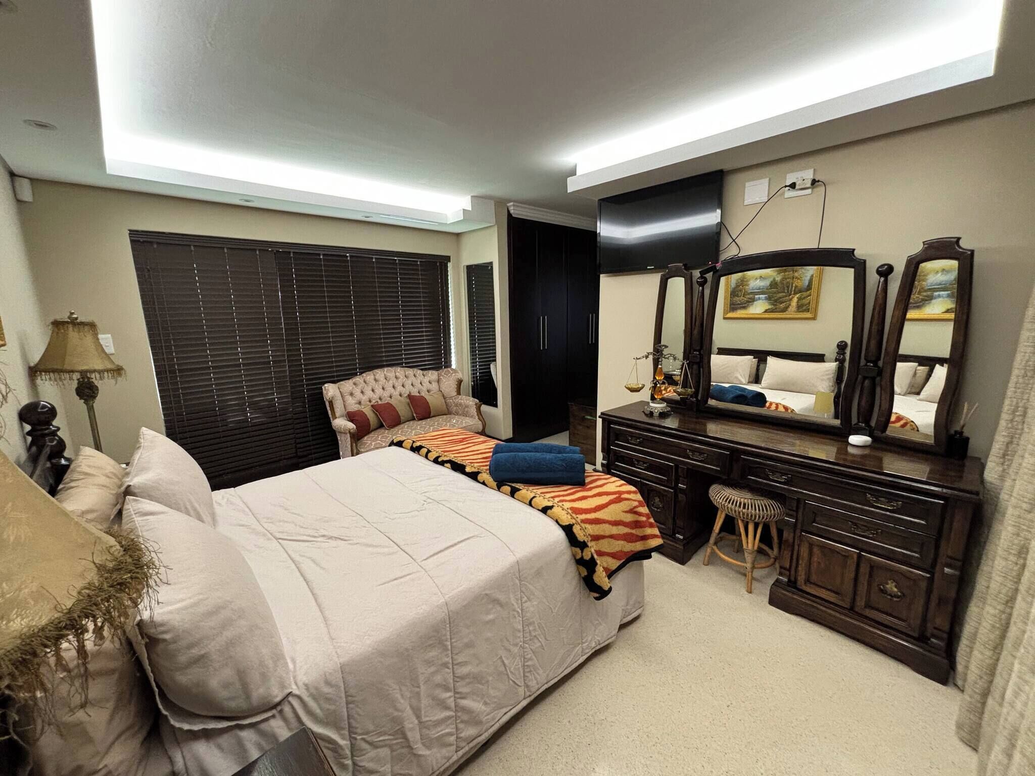 A bedroom with a large bed, a dresser, a mirror, and a window with blinds.