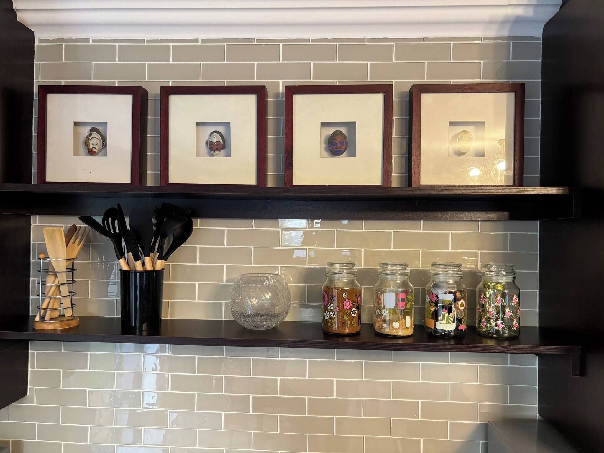 A kitchen shelf with framed pictures, a spice rack, and decorative jars.