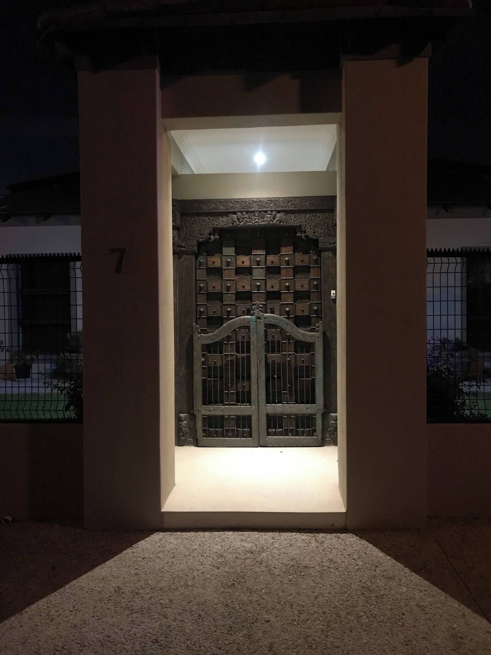 A gated entrance with a light source above the door, surrounded by a low wall and a number '7' on the left.