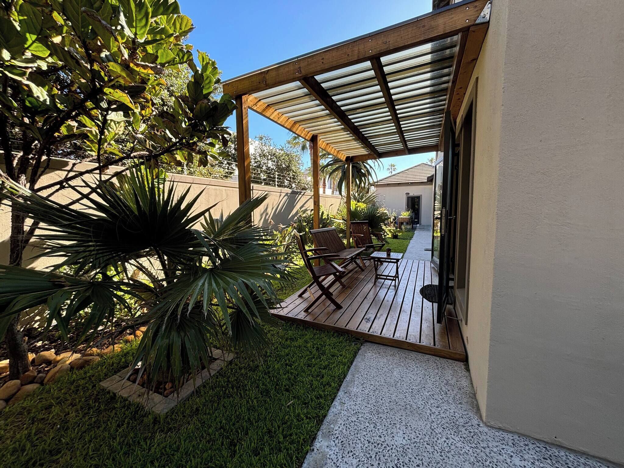 Un área de patio techada con cubierta de madera, mobiliario exterior y abundante vegetación.