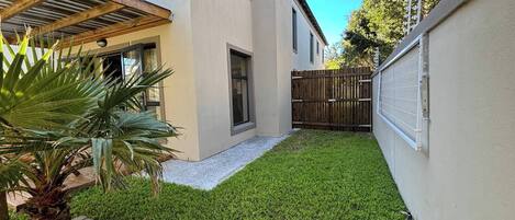 Un jardin bien entretenu avec une pelouse, une pergola en bois et un palmier.
