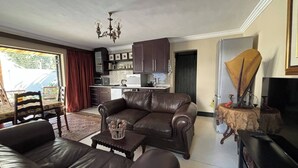 Ein Wohnzimmer mit einer Couch, einem Couchtisch und einem Fernseher. Es gibt eine Küchenzeile mit Schränken und Geräten.