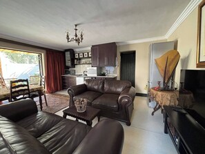 Ein Wohnzimmer mit einer Couch, einem Couchtisch und einem Fernseher. Es gibt eine Küchenzeile mit Schränken und Geräten.
