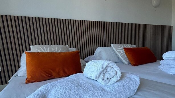 Hotellihuone, jossa on kaksi sänkyä, raidallinen pääty, valkoiset vuodevaatteet ja oranssit tyynyt.