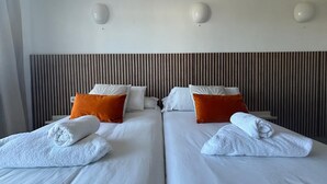 A hotel room with two beds, white linens, orange pillows, and white towels. - Es Grop Apartments (IB)