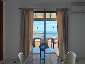A room with a table and chairs, a bottle of water, and a view of the sea through a glass door.