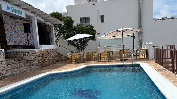 A swimming pool with a stone wall and a sign reading 'La Sencilla.' - Es Grop Apartments (IB)