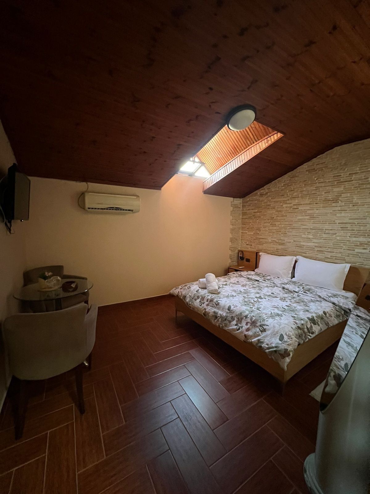 Un dormitorio con techo de madera, una cama con colcha estampada, una mesa redonda con sillas y un equipo de aire acondicionado montado en la pared.