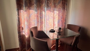 Comedor con una mesa de vidrio y dos sillas, piso de madera y cortina con diseño de mármol.