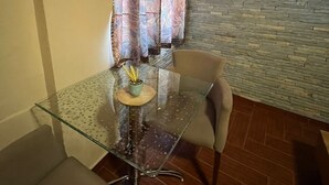 Un área de comedor con una mesa de vidrio, dos sillas, una planta en maceta y una pared de piedra.
