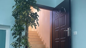 Una escalera que conduce a un piso superior, una puerta de madera oscura y una planta grande en maceta.