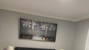 A neatly made bed with white bedding and a gray throw blanket, flanked by two bedside tables with lamps, in a room with a large painting on the wall.
