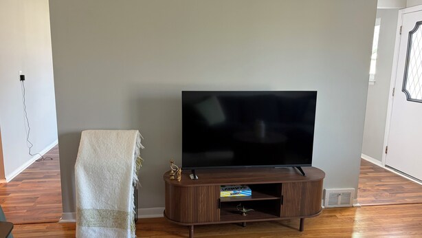 A living room with a flat-screen TV on a wooden stand, a white throw blanket, and a box of tissues.