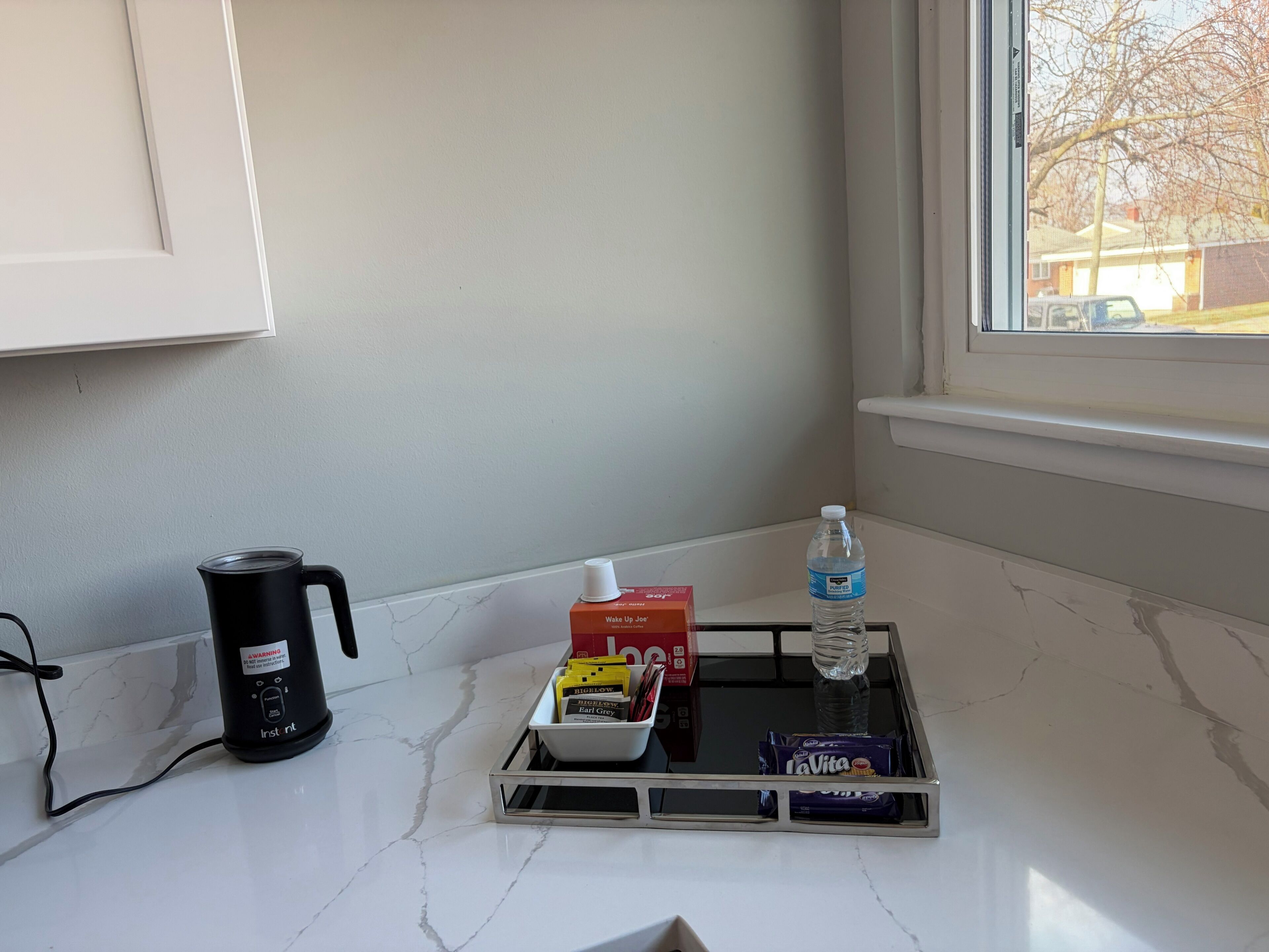 A kitchen counter with a coffee maker, a water bottle, and a tray with food items.