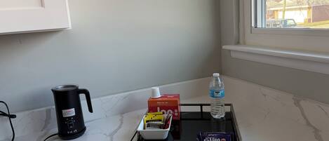 A kitchen counter with a coffee maker, a water bottle, and a tray with food items.