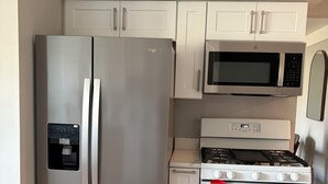 Une cuisine équipée d’un réfrigérateur en acier inoxydable, d’un four à micro-ondes, d’une cuisinière et de meubles de rangement blancs.