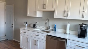 A modern kitchen with white cabinetry, a stainless steel dishwasher, and a coffee maker.