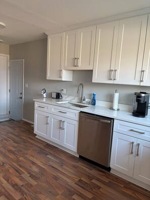 A modern kitchen with white cabinetry, a stainless steel dishwasher, and a coffee maker.