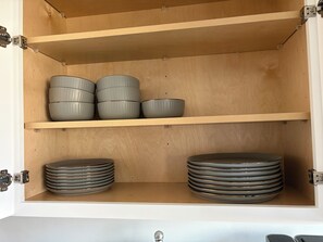 A cabinet with two shelves, one holding stacked bowls and the other holding stacked plates. - Adorable 2-bedroom house with AC in welcoming Westland (Westland)