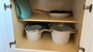 A kitchen cabinet with two shelves, one holding a frying pan and the other containing two pots.