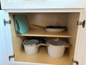 A kitchen cabinet with two shelves, one holding a frying pan and the other containing two pots.