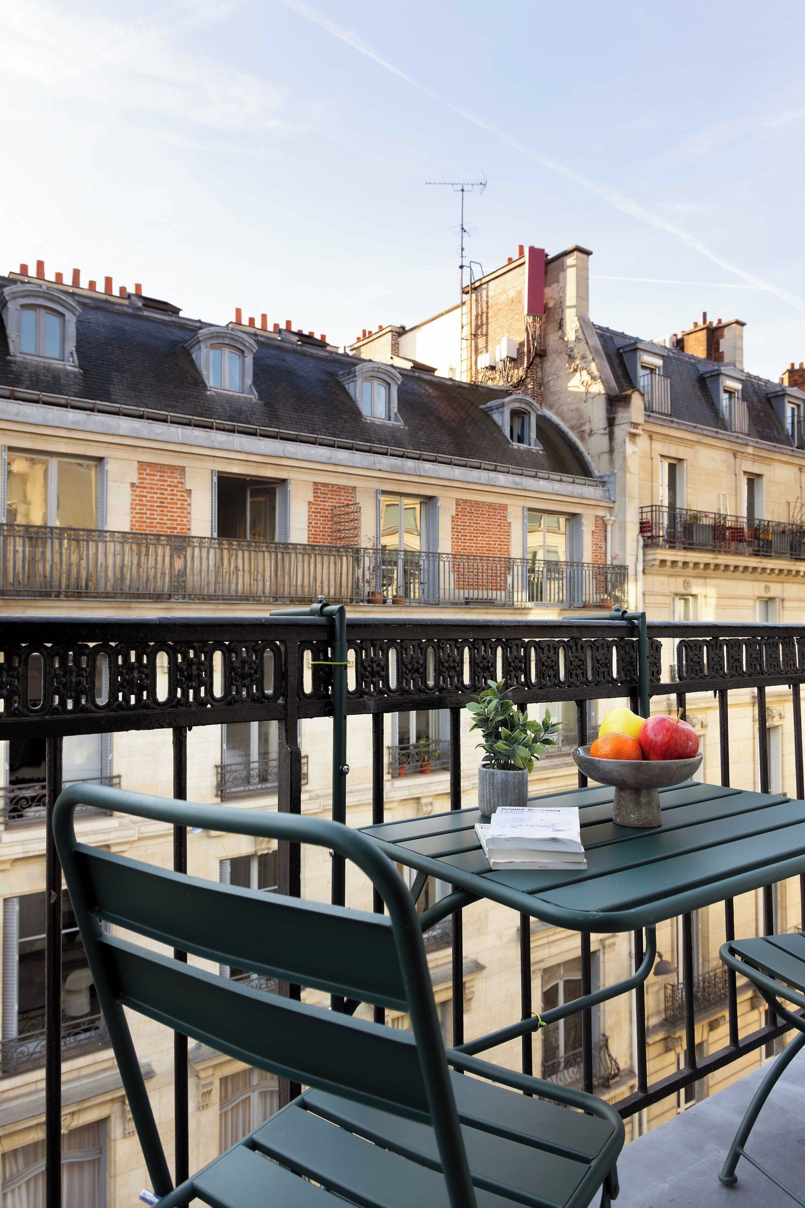 A balcony with a table, chairs, a bowl of fruit, and a potted plant.