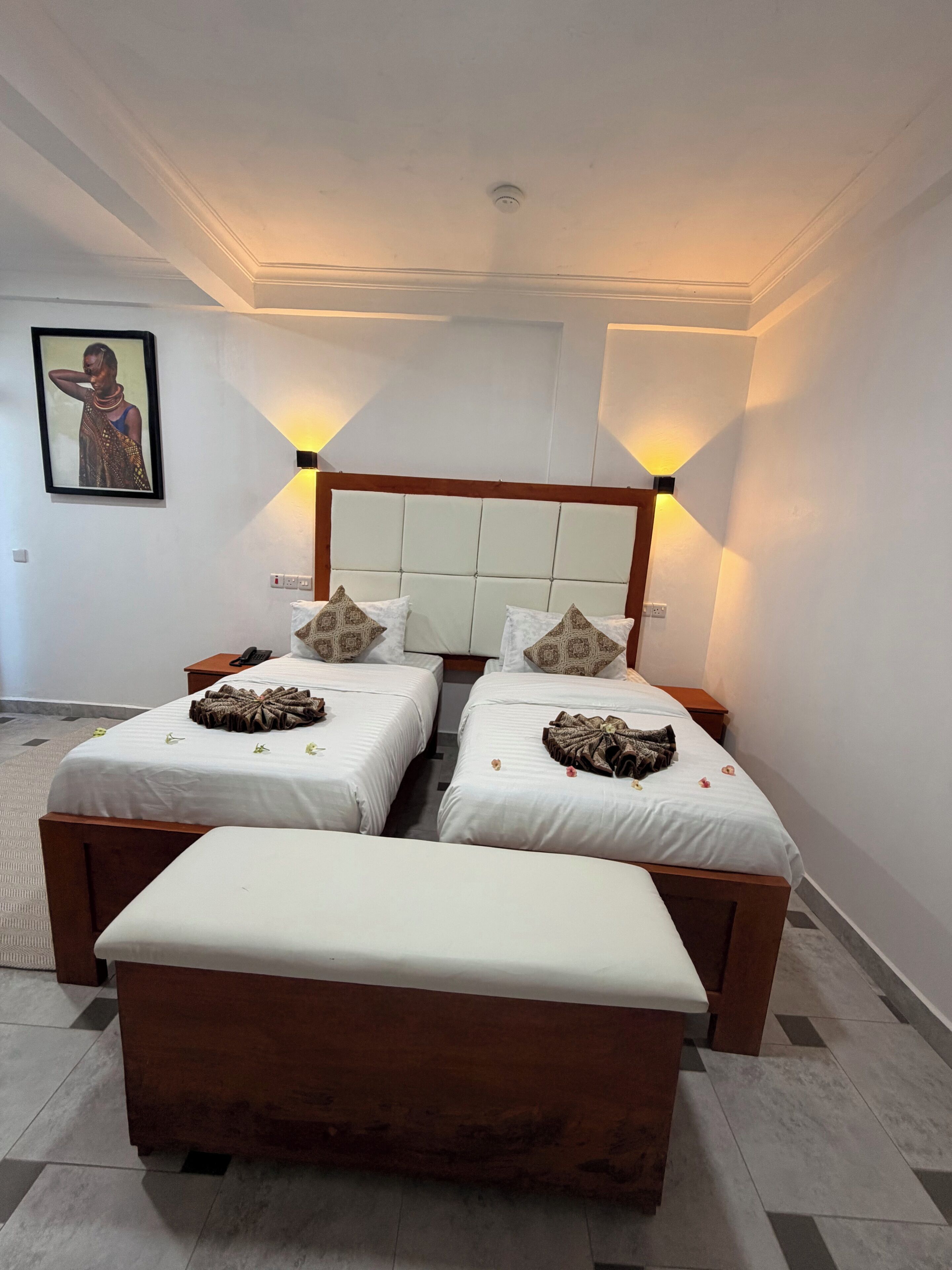 Una habitación de hotel con dos camas individuales, un sofá cama más grande, un cabecero con un panel de color claro y un cuadro en la pared.