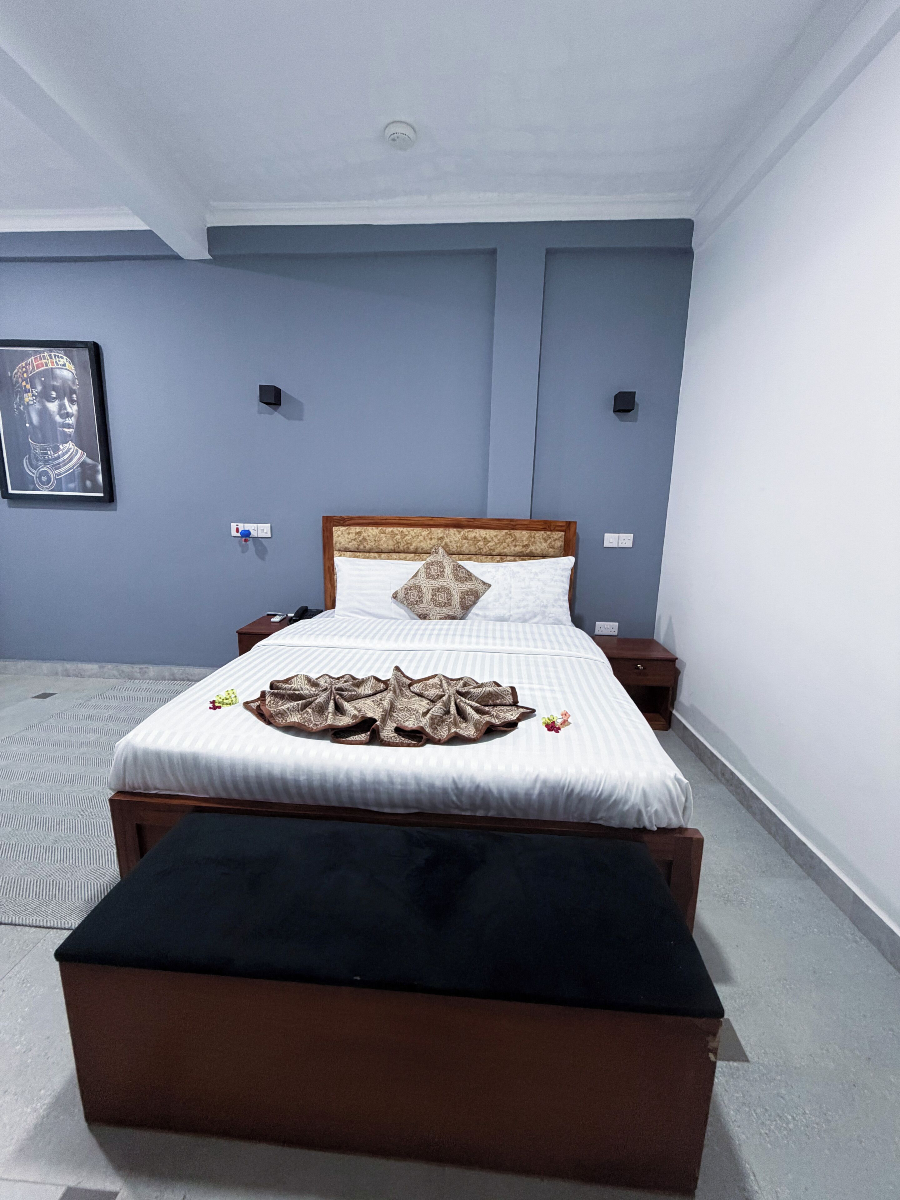 Un dormitorio con cama, mesitas de noche, cabecera, lámpara de pared e imagen enmarcada.