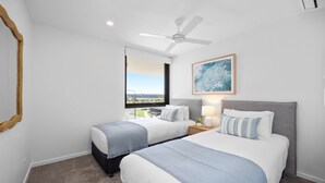A hotel room with two beds, a ceiling fan, a window with a view, and a framed artwork on the wall. - Poolside 2-bed Apartment at Lake Kawana (Sunshine Coast)