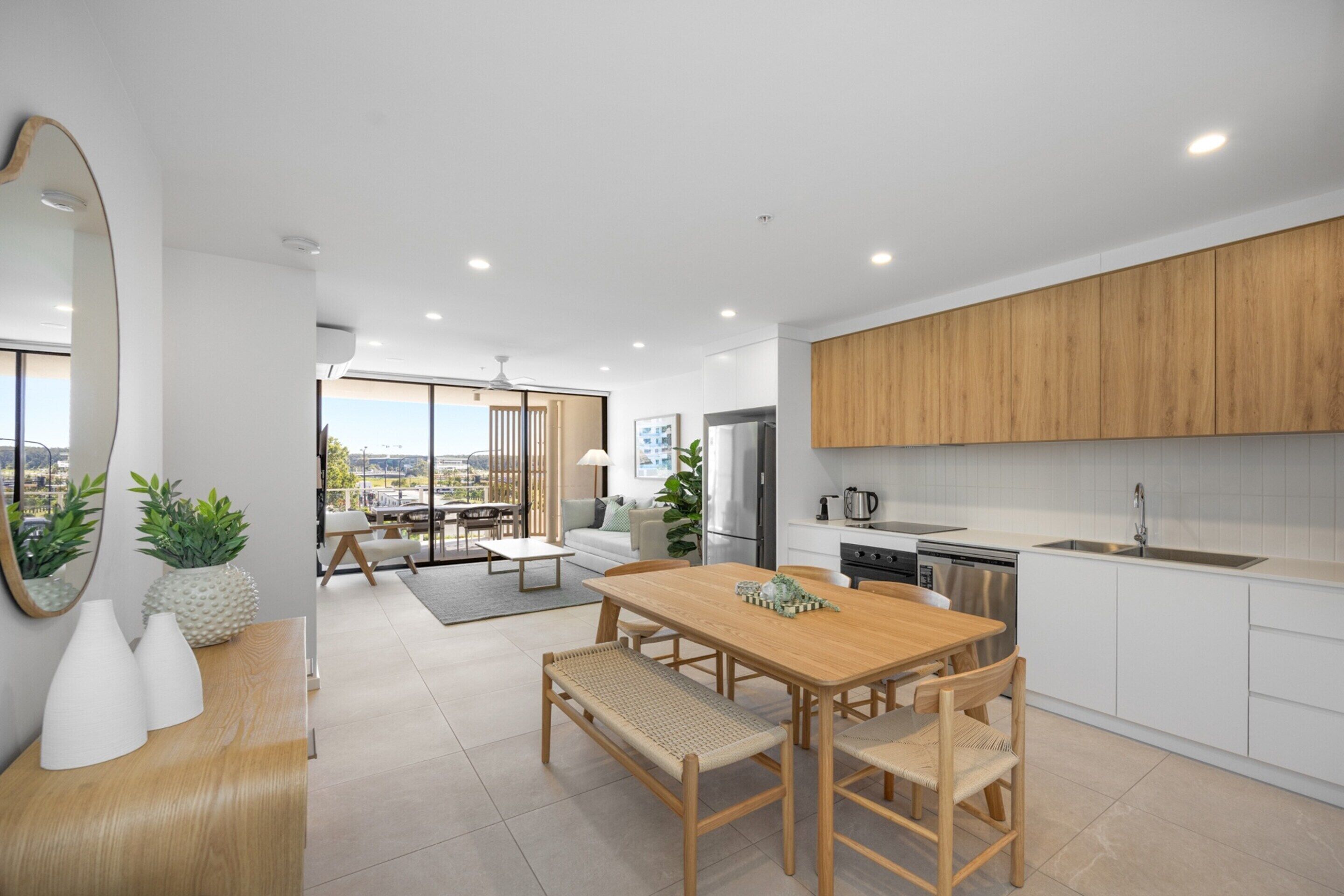 A modern kitchen with wooden cabinets, a dining area with a wooden table and chairs, and a view of the city through large windows.