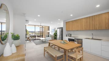 A modern kitchen with wooden cabinets, a dining area with a wooden table and chairs, and a view of the city through large windows.