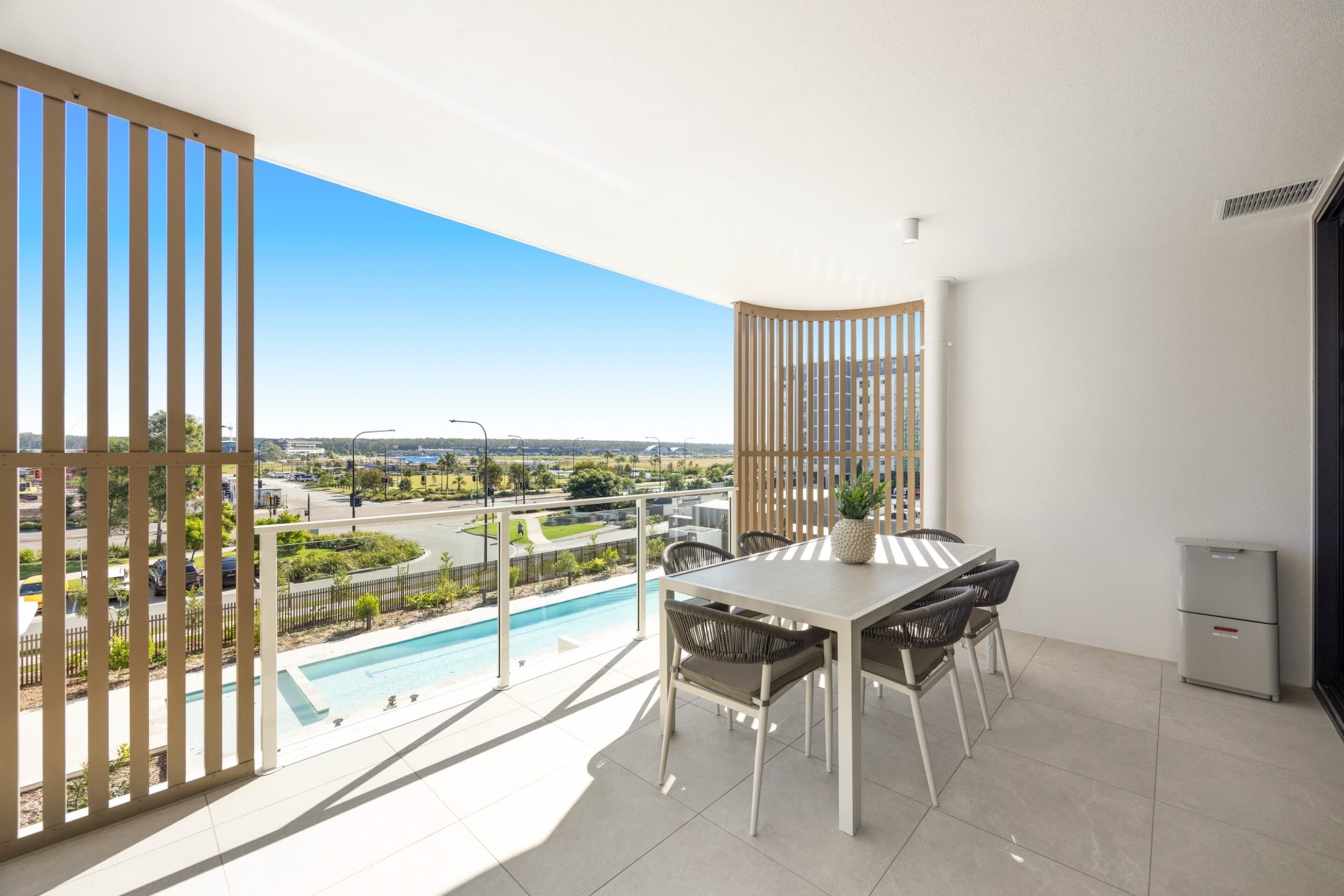Un balcon avec vue sur la piscine, une table à manger avec des chaises et un petit meuble.