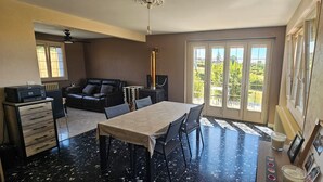 A dining area with a table and chairs, a sofa, a fireplace, and a view through large windows.