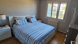Makuuhuone, jossa on sänky, yöpöytä, lamppu, ikkuna, patteri ja näkymä vihreälle alueelle.