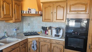 A kitchen with wooden cabinets, a gas stove, a microwave, and a kettle.