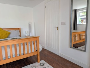 A bedroom with a wooden bed, a white door, a mirror, and a small bedside table. - Apartment Sleeps 3 With Garden & Free Parking (Didcot)