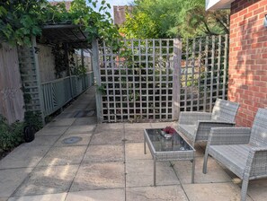 A patio with a glass-top table, wicker chairs, and a wooden fence. - Apartment Sleeps 3 With Garden & Free Parking (Didcot)