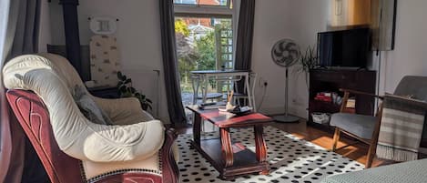 Una sala de estar con un sillón de cuero, una mesa de centro de madera, un tapete estampado, un televisor y una ventana con cortinas.