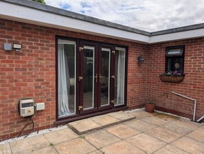 A brick building with a large glass door, a small window with a flower box, and a utility meter on the wall. - Apartment Sleeps 2 With Garden & Free Parking (Didcot)