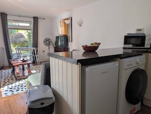 A compact kitchen with a washing machine, a microwave, and a dining area with a table and chairs. - Apartment Sleeps 3 With Garden & Free Parking (Didcot)