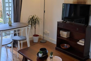 A living room with a TV on a stand, a dining table with chairs, a potted plant, and a bookshelf. - Apartment Sleeps 3 With Garden & Free Parking (Didcot)
