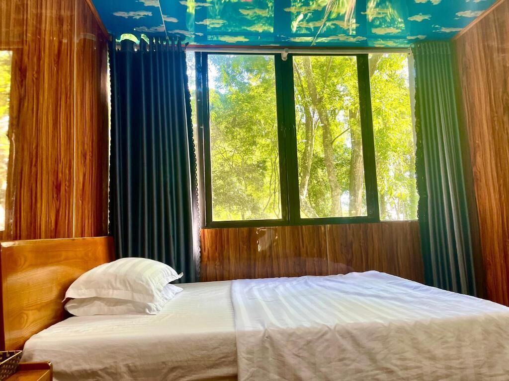 A room with a bed, curtains, and a view of trees through the window.