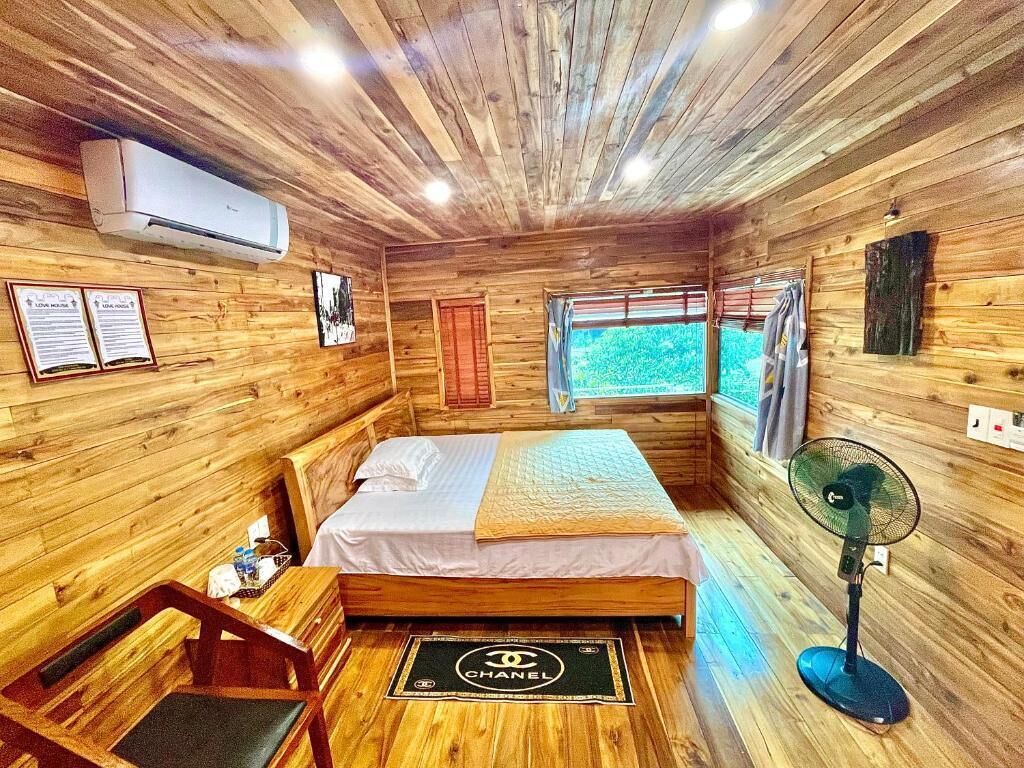 Een houten kamer met een bed, een ventilator en een raam.