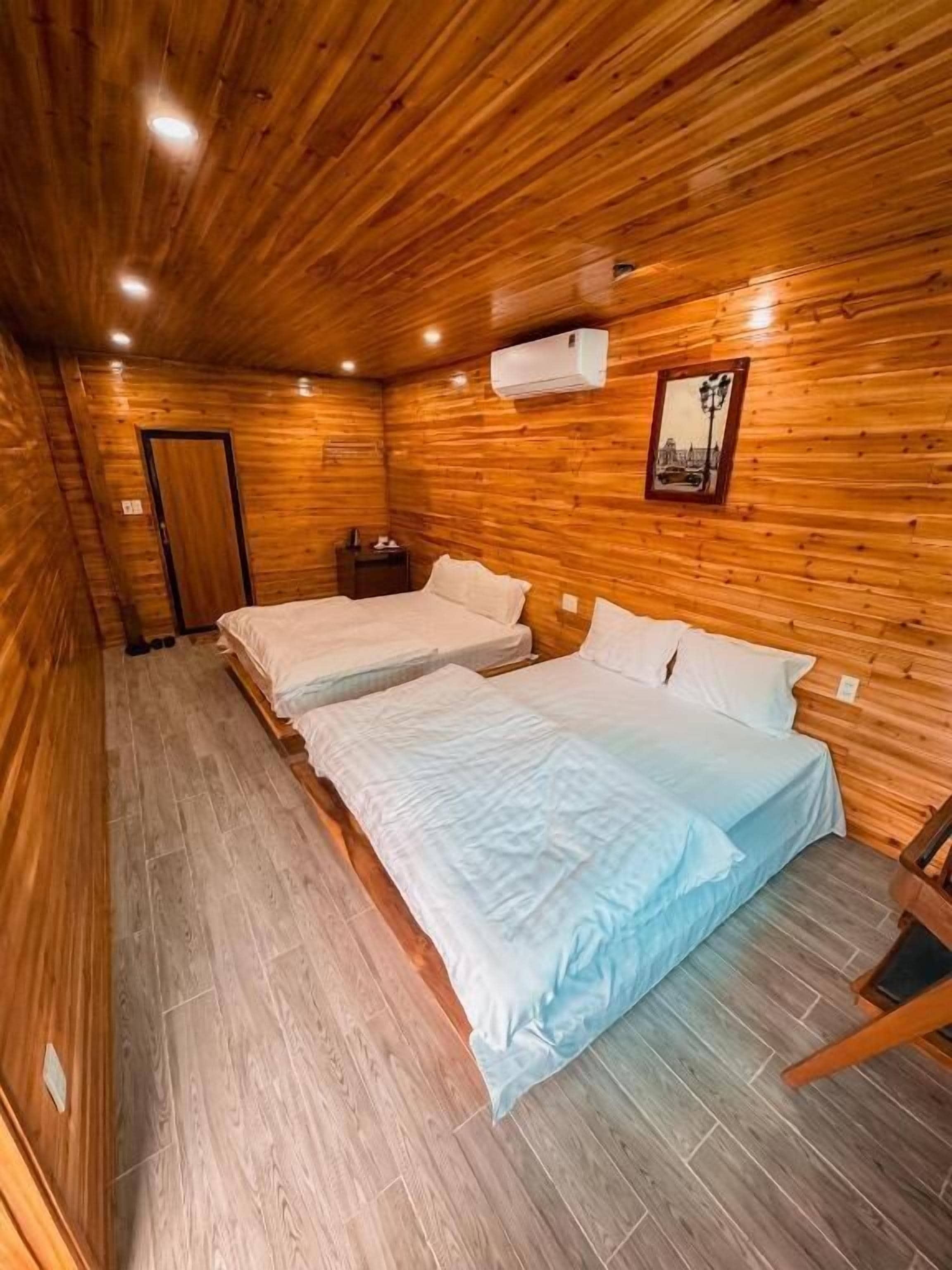 A wooden-paneled room with two beds, a nightstand, and a framed picture on the wall.