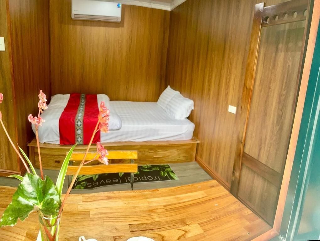 A compact room with a bed, wooden walls, a small table, and a window.